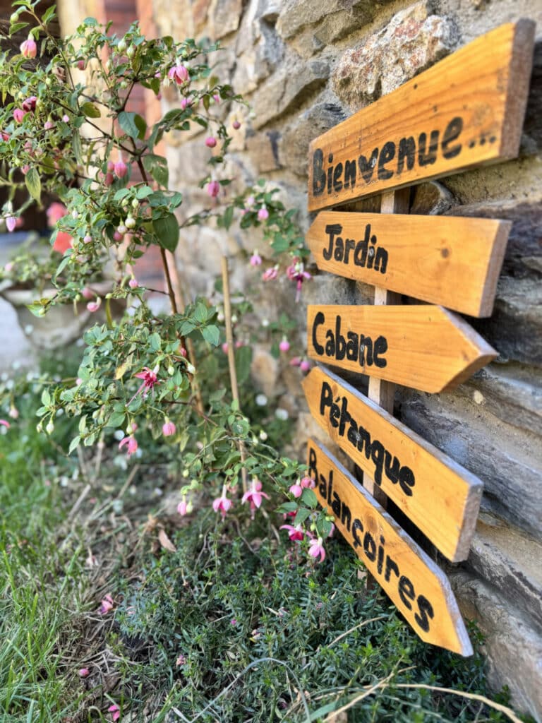 Panneau en bois “Bienvenue, Jardin, Cabane, Pétanque, Balançoires” devant la maison d’hôtes Chez Delphine à Doizieux.