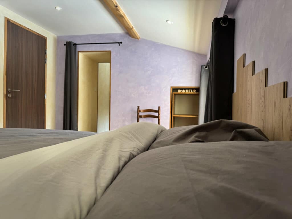 Chambre Côté Cabane à Doizieux : vue depuis le lit, tête de lit en bois, tons lavande – Parc du Pilat.