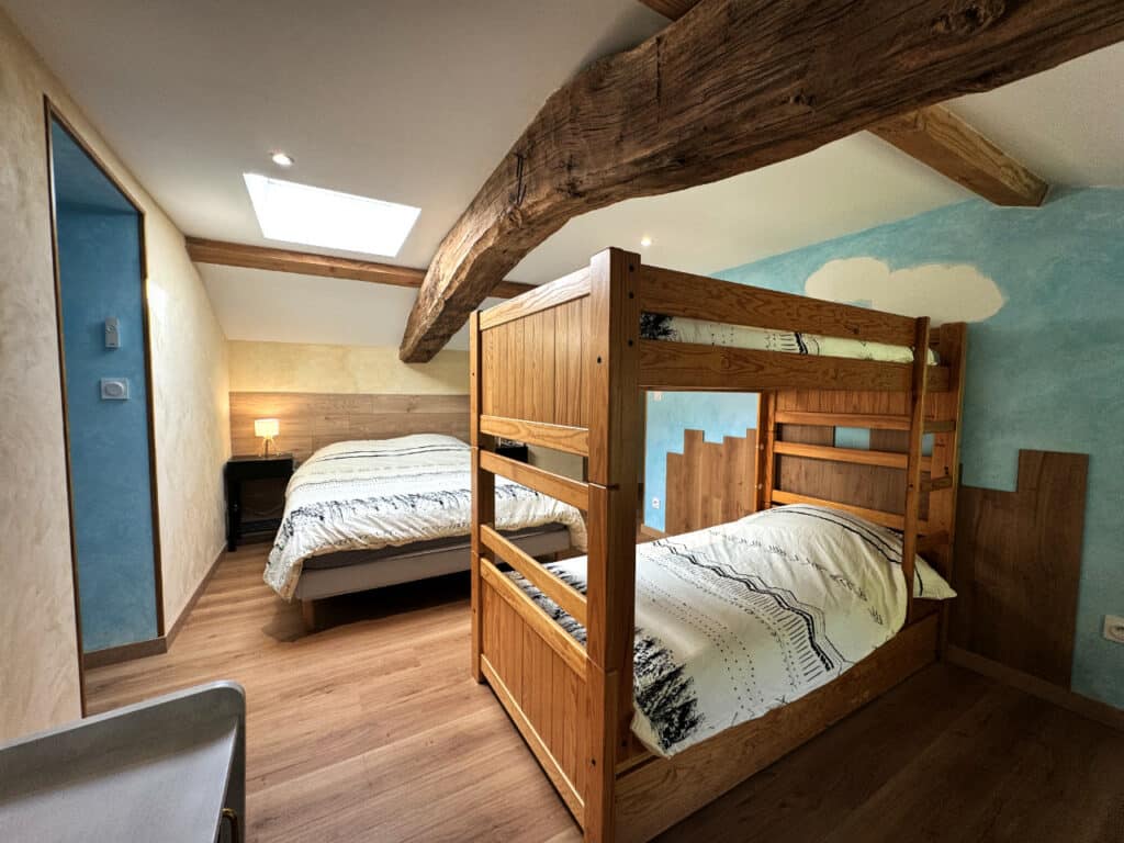 Chambre familiale « Près du Barrage » avec lit double et lits superposés sous poutres apparentes.