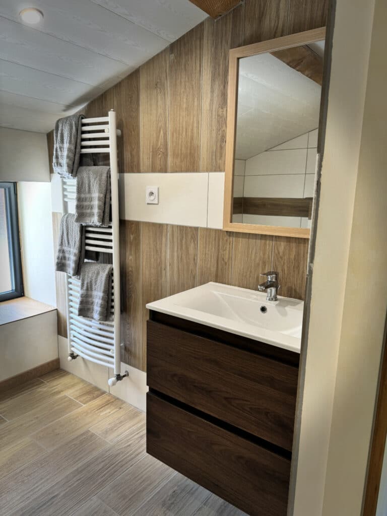 Vasque en bois avec miroir et sèche-serviettes blanc dans la salle de bain de la chambre Côté Jardin.