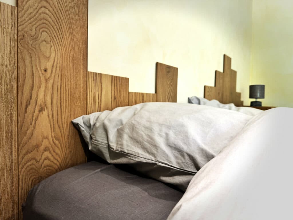 Détail d’une tête de lit en bois massif dans la chambre côté jardin du gîte, réalisée sur mesure par un artisan local.